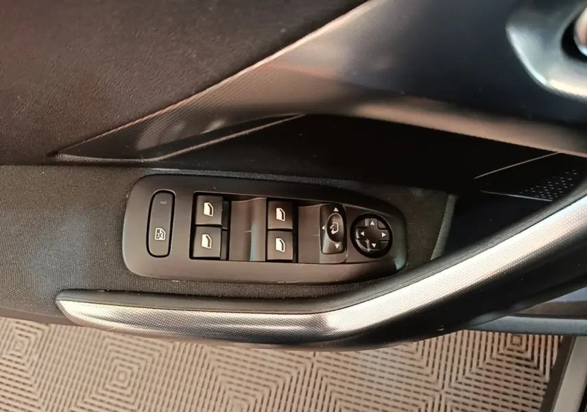 Gros plan sur les commandes des vitres et rétroviseurs côté gauche de la Peugeot 2008 noire, intérieur tissu.