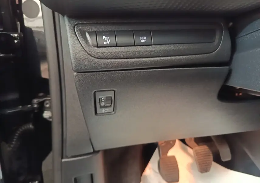 Vue intérieure côté gauche du tableau de bord noir du Peugeot 2008 avec commandes de phares et pédales visibles.