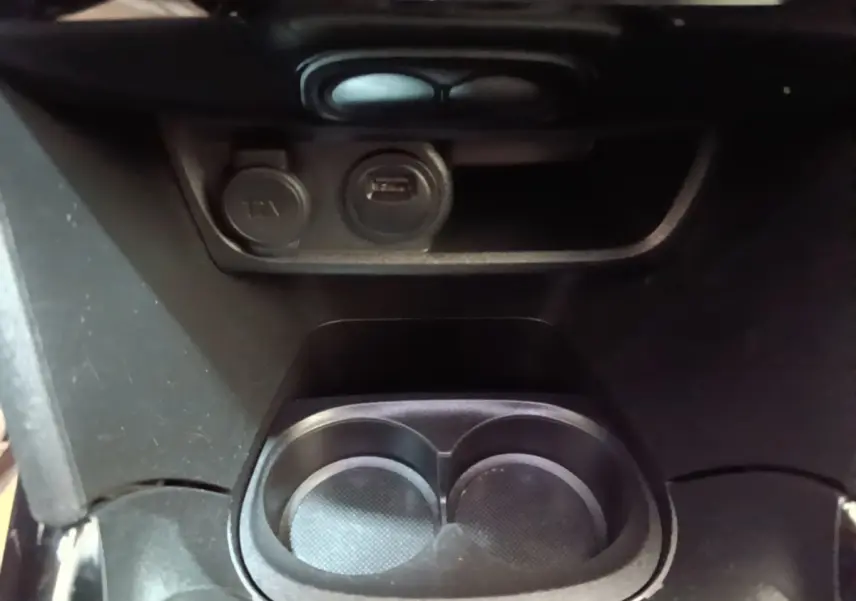 Gros plan sur la console centrale noire du Peugeot 2008 avec porte-gobelets et prises 12V et USB visibles.
