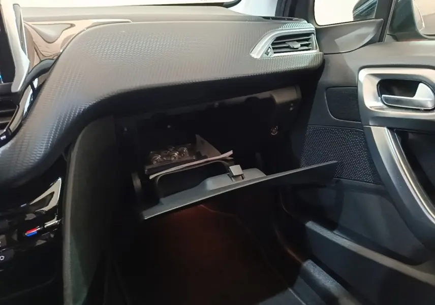 Intérieur côté passager du Peugeot 2008 noir, avec boîte à gants ouverte et tableau de bord texturé noir.