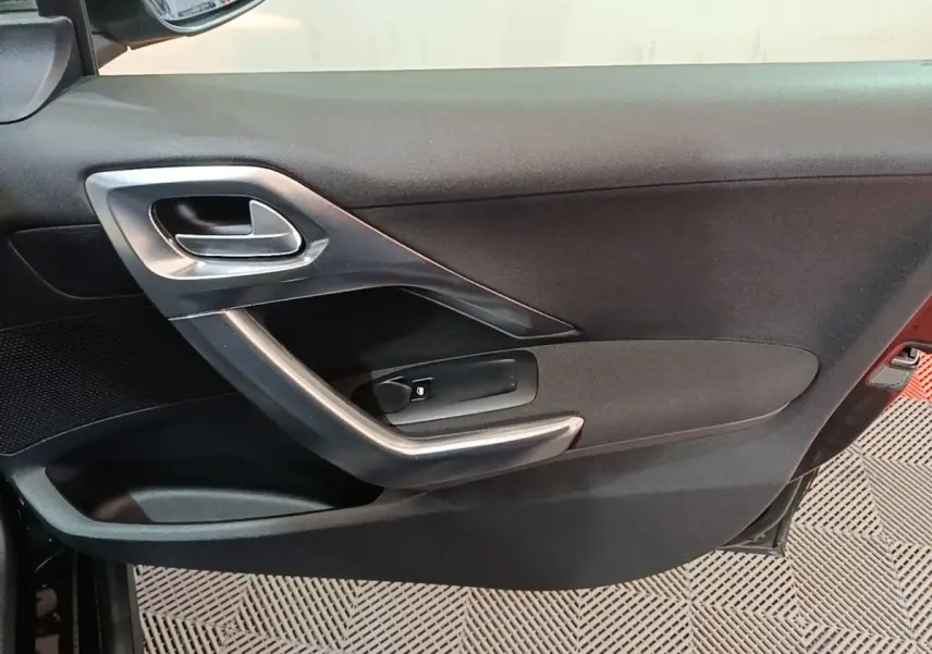 Intérieur de la porte côté conducteur d'une Peugeot 2008 noire, avec poignée argentée et commande de lève-vitre.