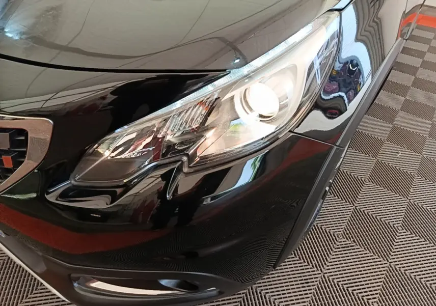 Gros plan sur le phare avant droit d’un Peugeot 2008 noir brillant, avec calandre et pare-chocs visibles.
