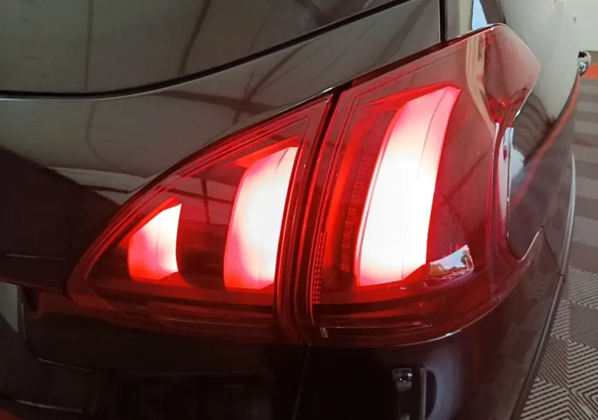 Gros plan sur le feu arrière droit rouge d’une Peugeot 2008 noire, soulignant ses lignes modernes et brillantes.