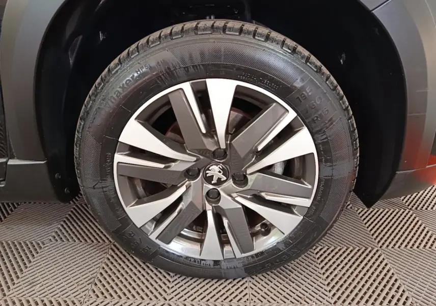 Gros plan sur la roue avant droite d'un Peugeot 2008 noir, mettant en valeur la jante alliage au design moderne.