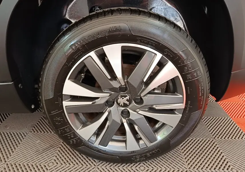 Gros plan sur la roue avant droite d’un Peugeot 2008 noir, avec jante alliage et logo lion au centre.