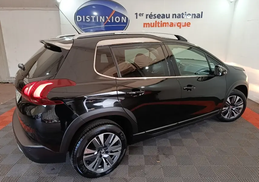 Vue 3/4 arrière droite d’un Peugeot 2008 noir brillant avec jantes alliage et rails de toit chromés en intérieur showroom.