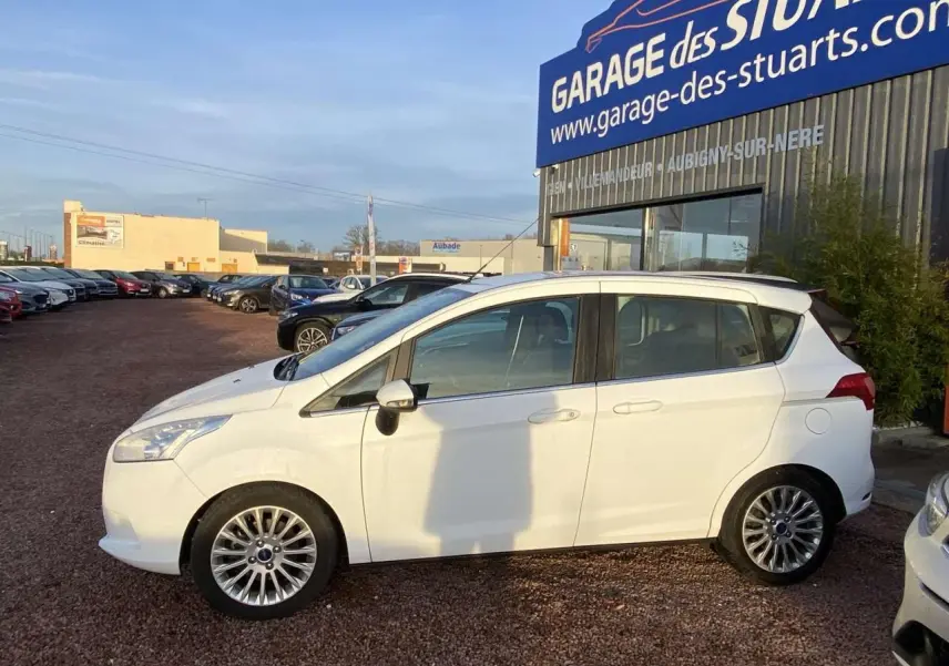 Ford B-MAX blanc vue de profil côté gauche, stationné devant un garage avec jantes alliage 16 pouces.