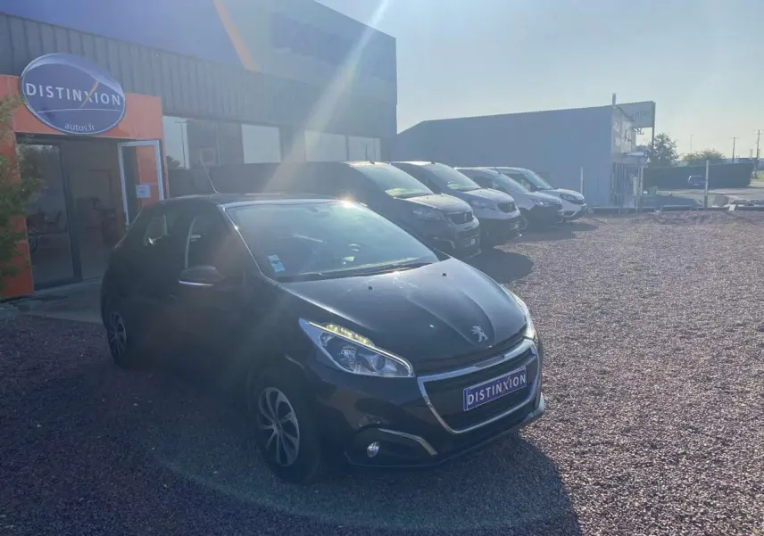 Peugeot 208 noire vue en 3/4 avant gauche sur un parking devant un bâtiment avec enseigne Distinxion.