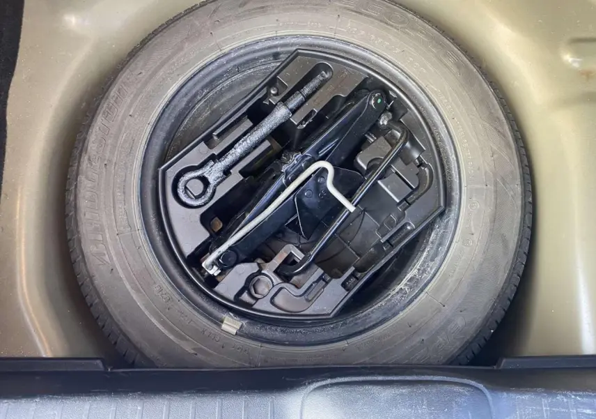 Gros plan sur la roue de secours acier 15 pouces et le cric dans le coffre d'une Peugeot 208 noire 2016.