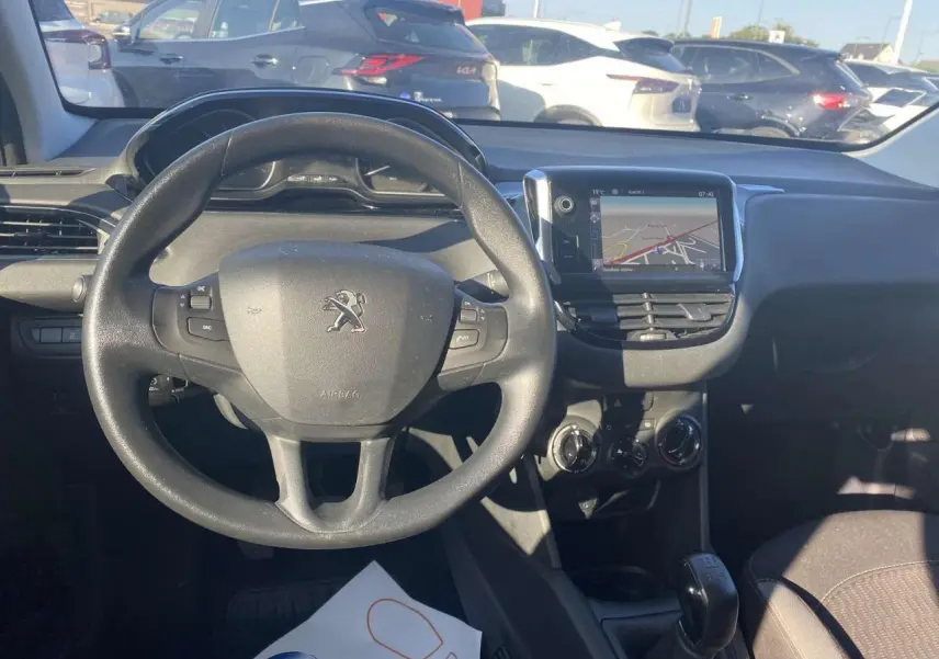 Vue de face de l'intérieur d'une Peugeot 208 noire, volant multifonction et écran tactile GPS au centre du tableau de bord.