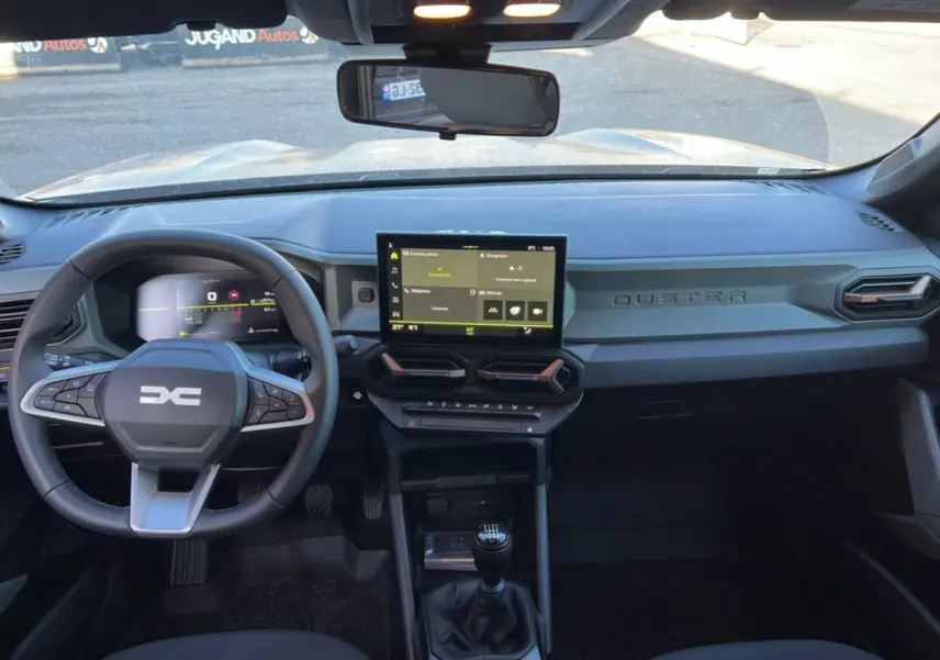 Vue intérieure du tableau de bord du Dacia Duster 2024 brun terracotta avec écran tactile et boîte manuelle visible.