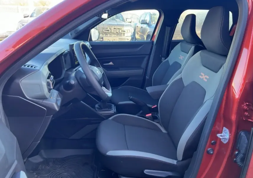 Vue intérieure côté conducteur du Dacia Duster 2024 brun terracotta, montrant les sièges sport et le tableau de bord moderne.
