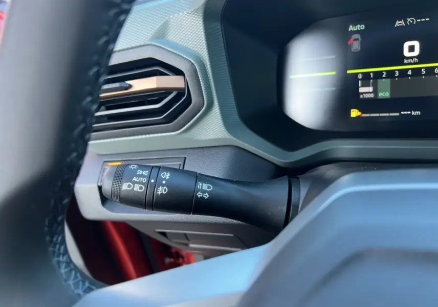 Détail du commodo d'éclairage et tableau de bord numérique du Dacia Duster 2024 brun terracotta, vue intérieure côté conducteur.