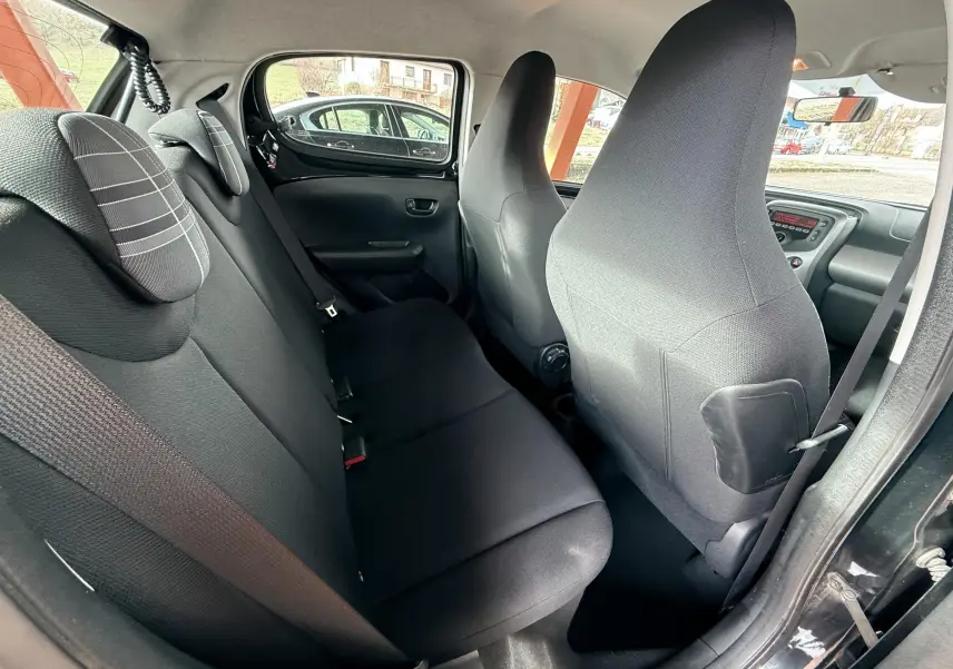 Vue intérieure arrière côté droit de la Peugeot 108 noire de 2018, montrant les sièges en tissu gris noir et la portière ouverte.