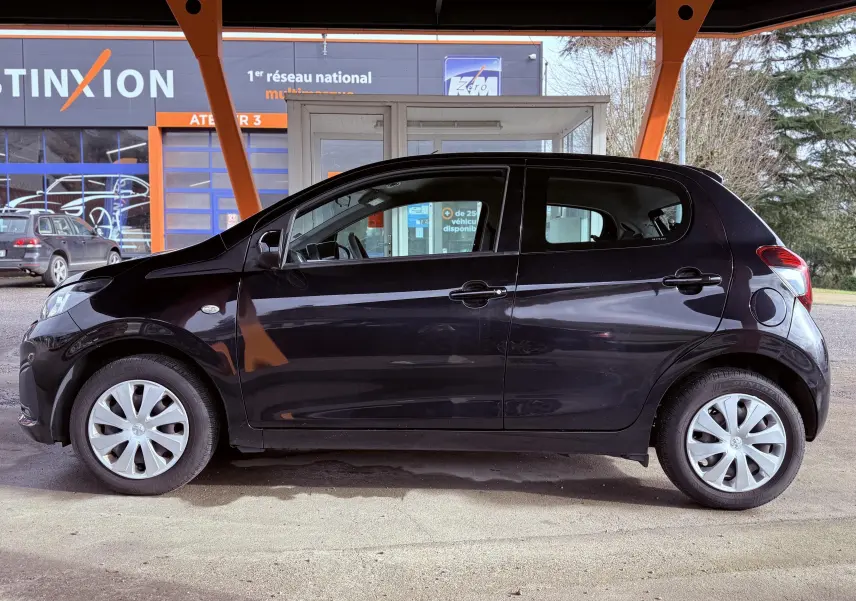 Profil latéral droit d'une Peugeot 108 noire 5 portes garée sous un abri avec jantes argentées et vitres teintées.