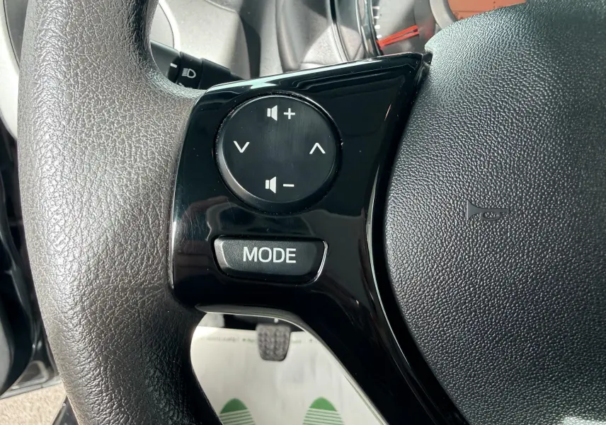 Gros plan sur les commandes audio noires du volant d'une Peugeot 108 2018, avec tableau de bord en arrière-plan.