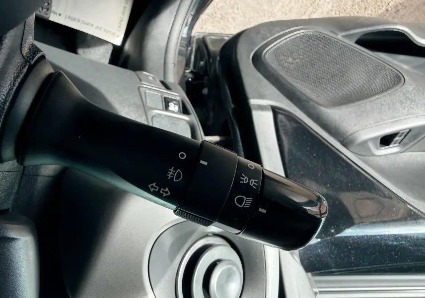 Gros plan sur la commande des phares et clignotants à gauche du volant dans l'habitacle noir d'une Peugeot 108.