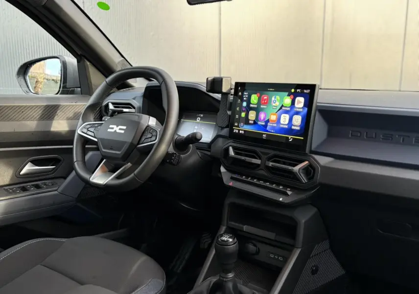 Vue intérieure côté conducteur du Dacia Duster 2024 beige Sandstone, avec volant multifonction et écran tactile central.