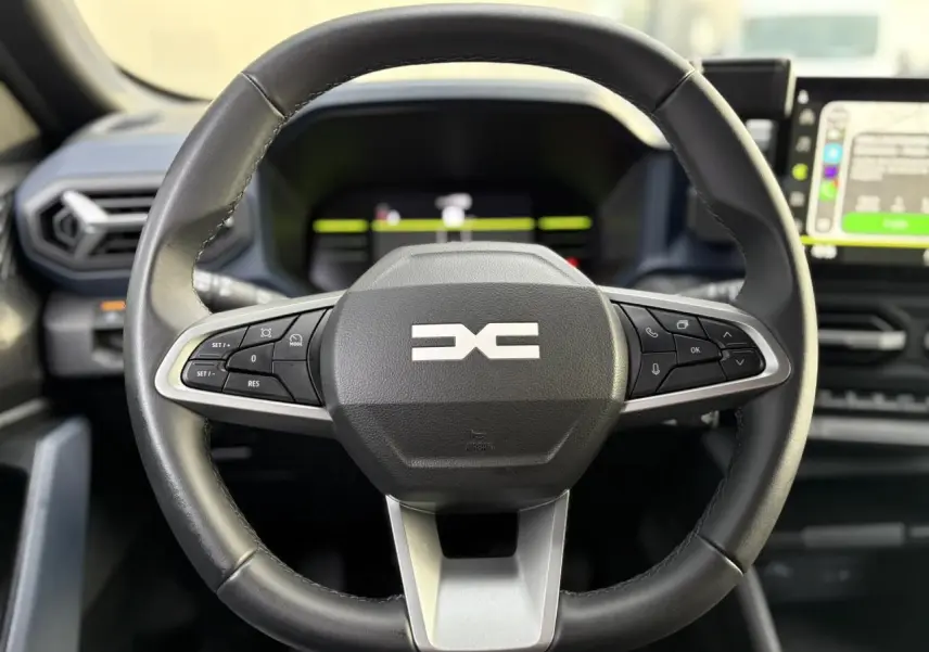 Gros plan sur le volant noir soft feel du Dacia Duster 2024 avec commandes intégrées et tableau de bord digital.