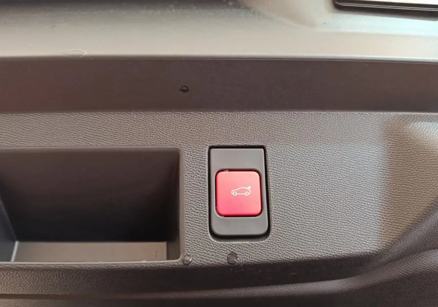 Bouton rouge d'ouverture électrique du coffre sur panneau intérieur noir, vue rapprochée sans indication extérieure visible.