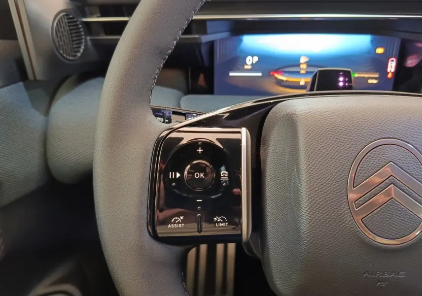 Gros plan sur le volant cuir gris du Citroën C5 Hybride avec commandes multifonctions et tableau de bord numérique lumineux.