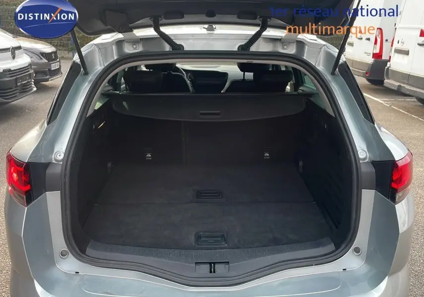 Coffre ouvert d'une Renault Mégane Break gris Highland Metal vue arrière en extérieur sur parking.