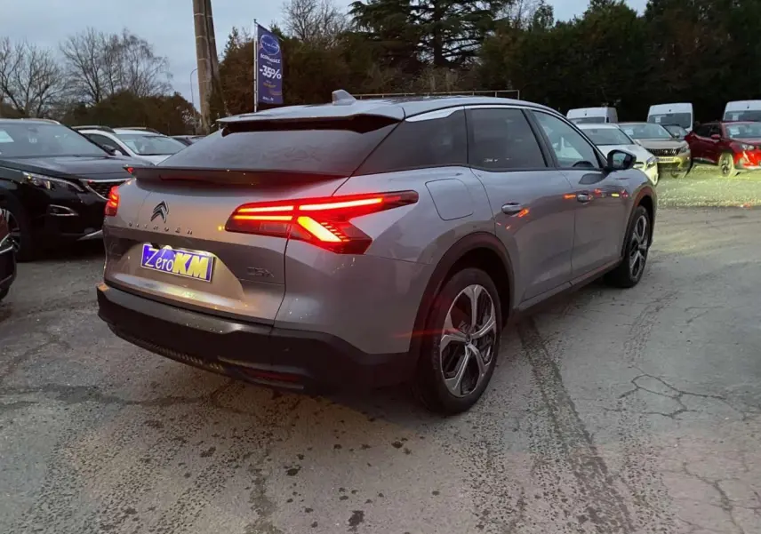 Vue 3/4 arrière droite d'une Citroën C5 X gris Artense métallisé avec feux arrière LED distinctifs allumés.