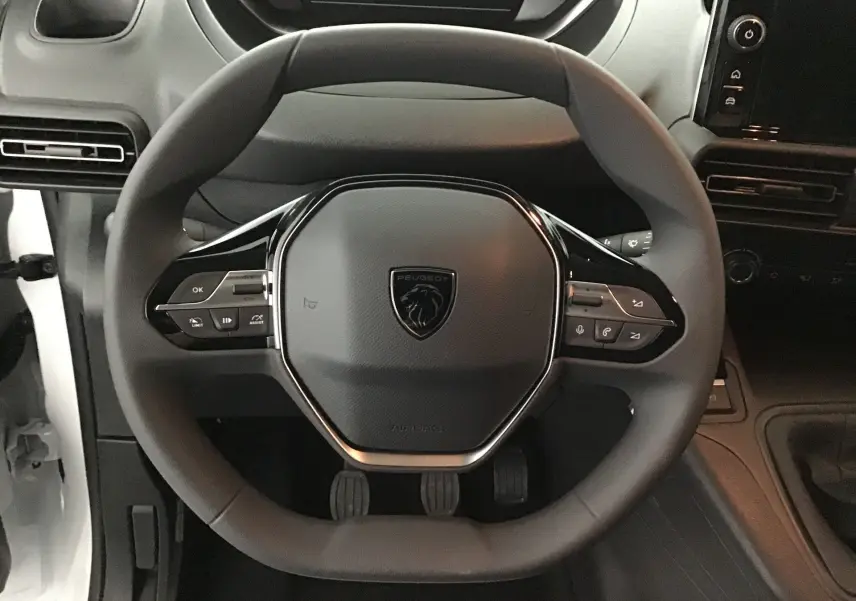 Vue frontale du volant noir du Peugeot Partner 2025 avec commandes intégrées et tableau de bord partiel visible.