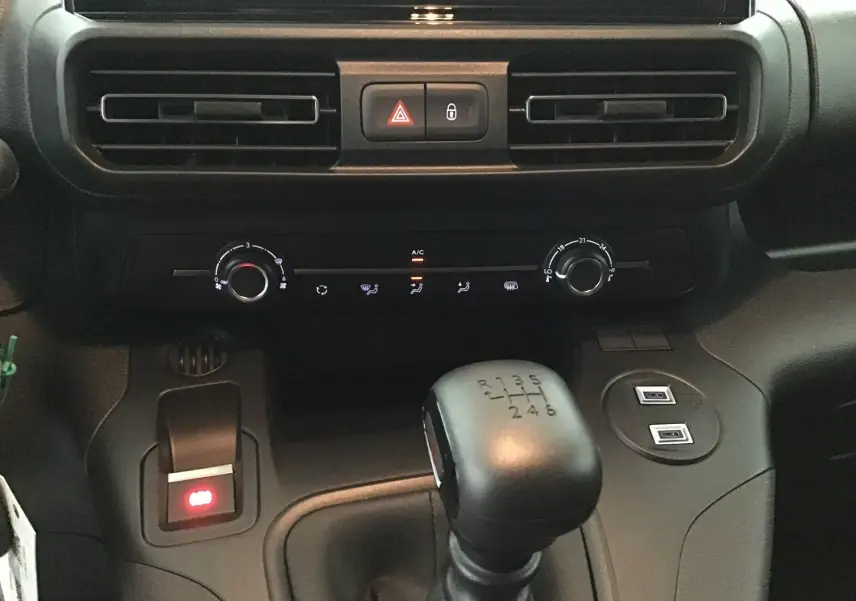 Vue rapprochée de la console centrale du Peugeot Partner 2025, montrant la boîte manuelle noire et les commandes de climatisation.