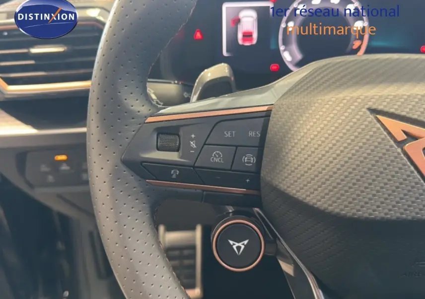 Gros plan sur le volant perforé gris avec logo CUPRA, boutons de commande et tableau de bord numérique en arrière-plan.