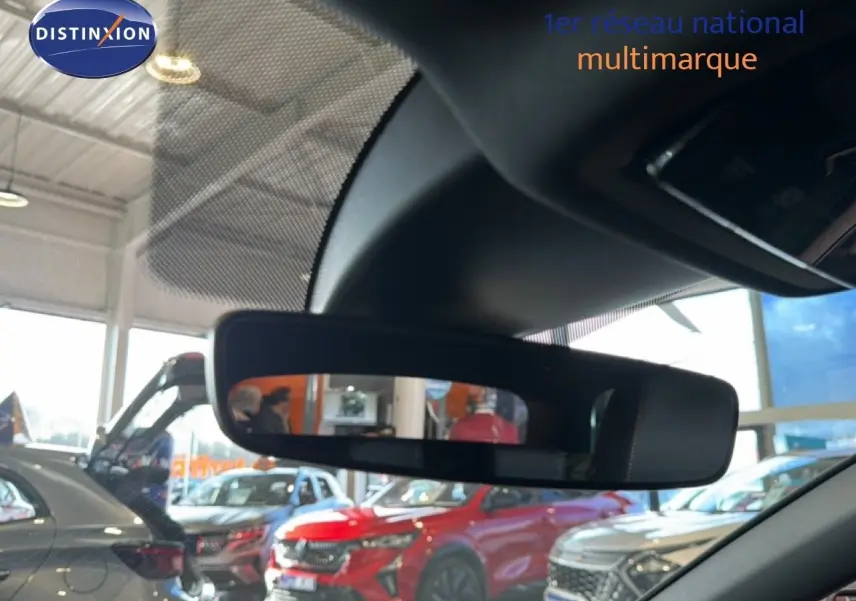 Rétroviseur intérieur montrant en reflet plusieurs véhicules en concession, dont un SUV rouge et une voiture grise.