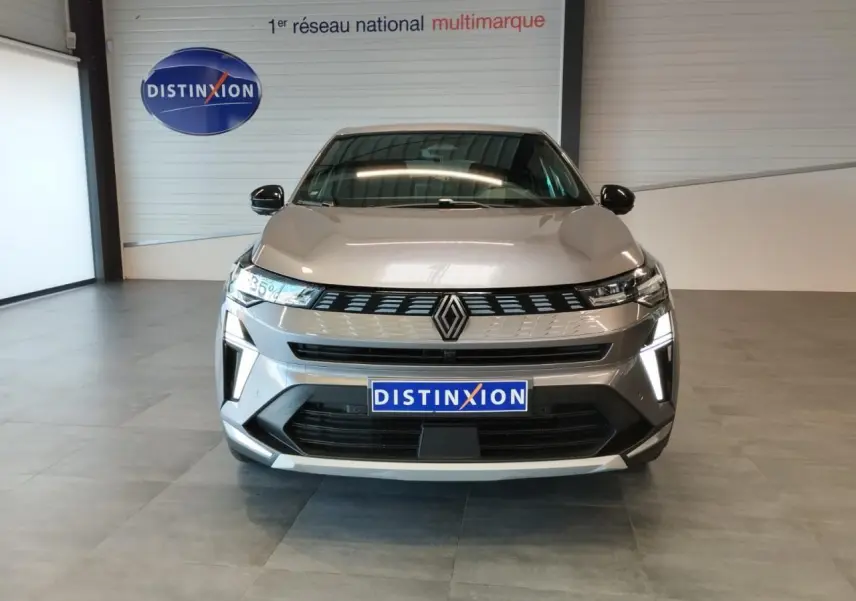 Vue de face du Renault Symbioz gris Cassiopée avec calandre 3D et feux LED verticaux allumés en intérieur showroom.
