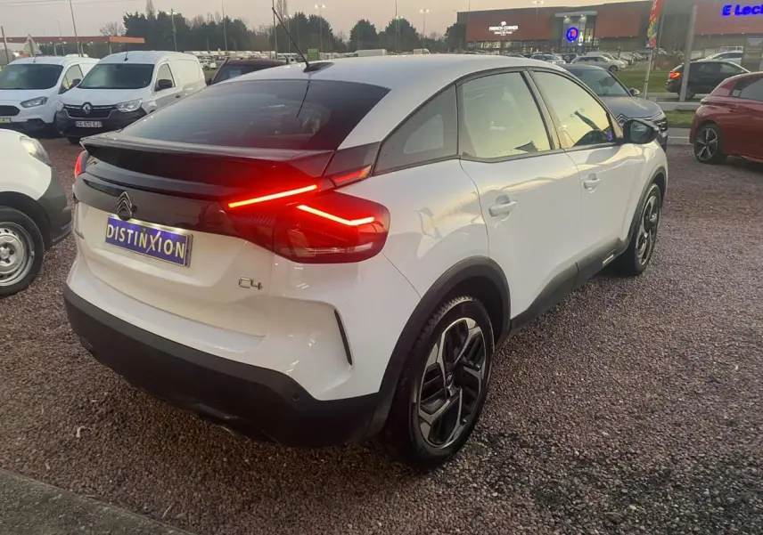 Vue 3/4 arrière droite d'une Citroën C4 blanche avec feux arrière LED allumés sur parking extérieur.