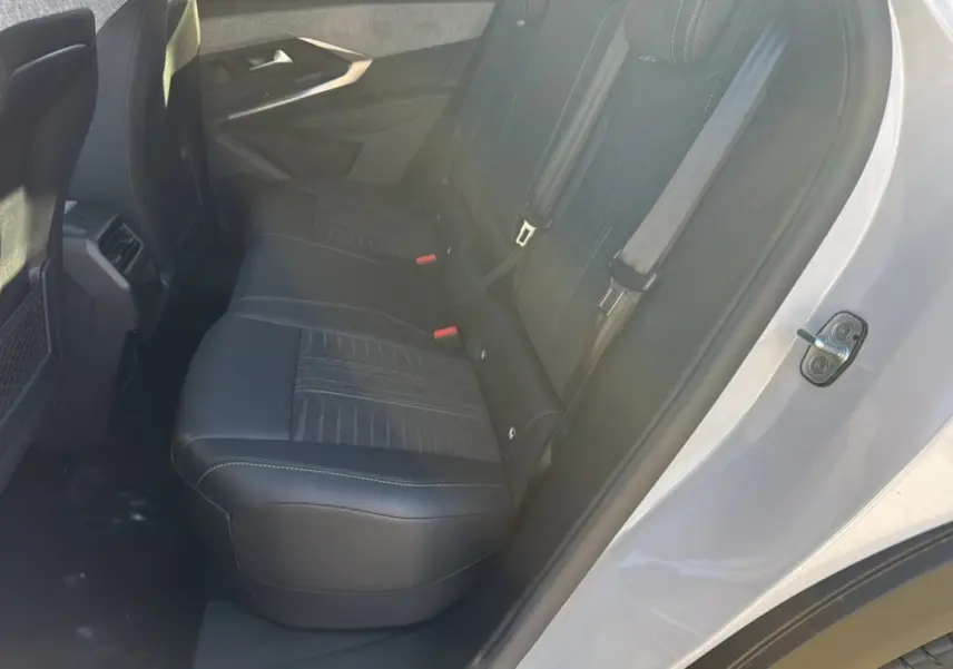 Vue intérieure côté arrière droit du Peugeot 3008 Hybrid 136 GT Plus blanc okénite, sièges en cuir noir avec surpiqûres.