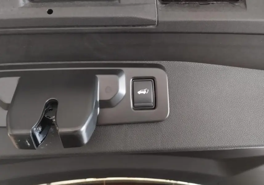 Bouton d'ouverture électrique du hayon sur la partie intérieure d'un Renault Symbioz gris Cassiopée, vue en gros plan.