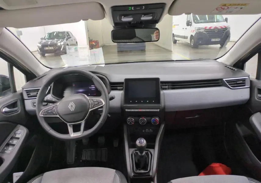 Vue intérieure avant de la Renault Clio 2024 avec tableau de bord gris, volant multifonction et écran tactile central.