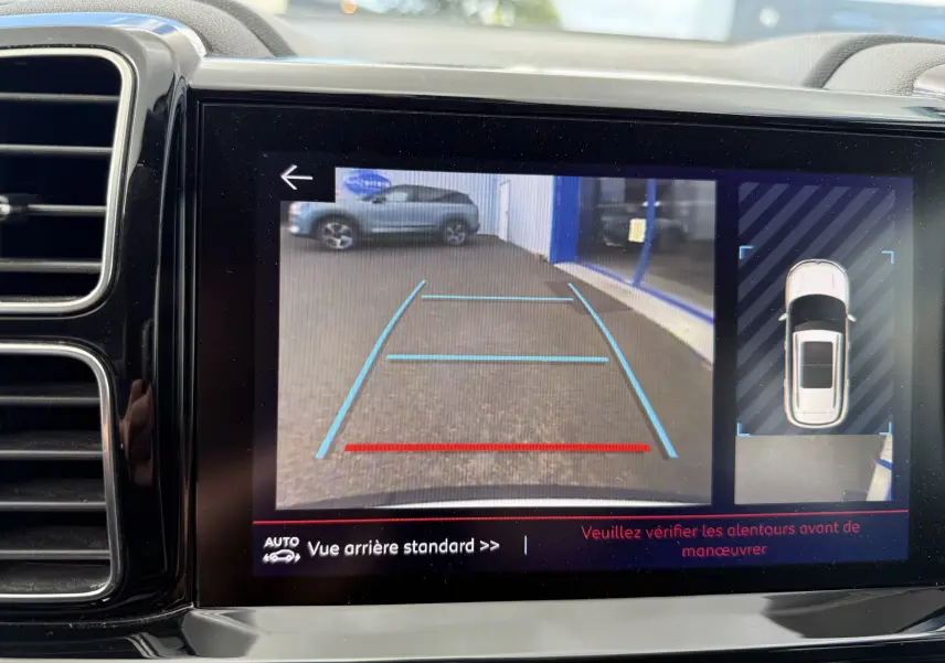 Écran de caméra de recul montrant une Citroën C5 Aircross blanche vue de dessus et arrière en stationnement.
