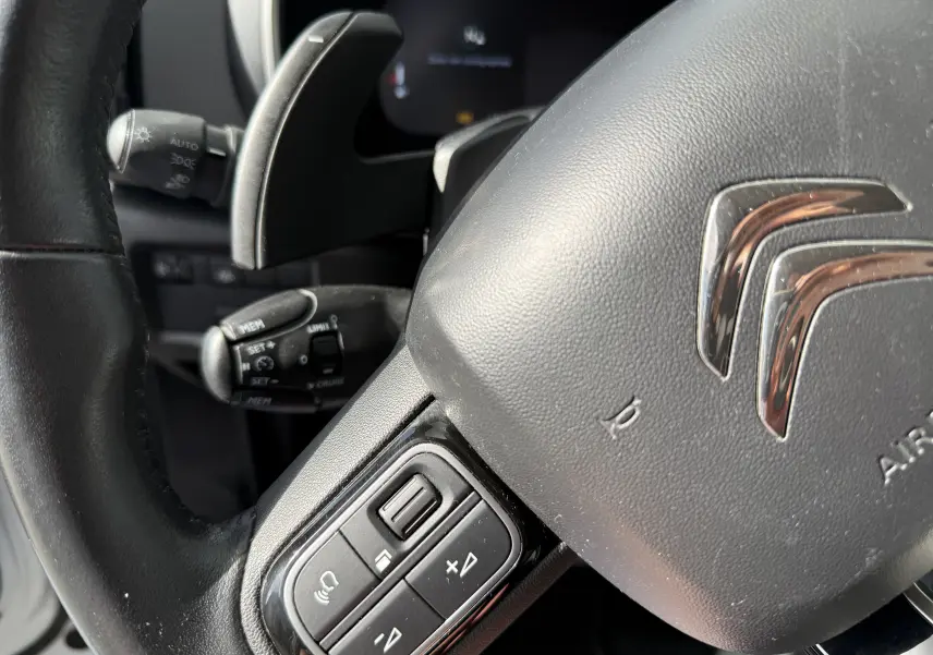 Gros plan sur le volant noir de Citroën C5 Aircross avec commandes intégrées et logo chromé au centre.