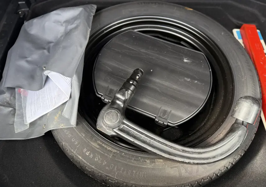 Gros plan sur la roue de secours avec attelage démontable et pochette grise dans le coffre du Citroën C5 Aircross blanc.