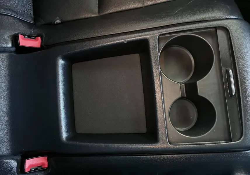 Gros plan sur la console centrale noire avec porte-gobelets et accoudoir en cuir dans une Mercedes Classe E 250 Coupé gris.