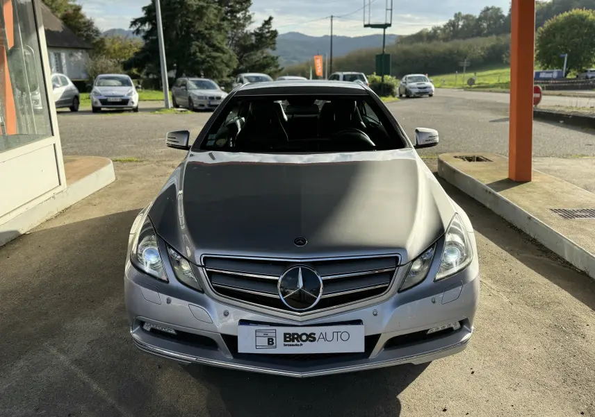 Vue avant d'une Mercedes Classe E 250 Coupé gris métallisé garée sous un auvent avec logo bien visible.