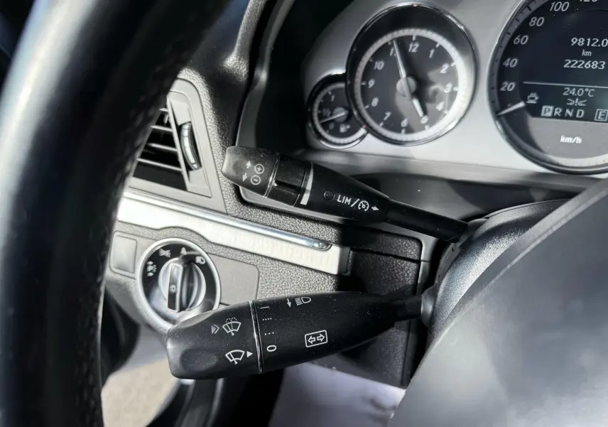 Gros plan sur le tableau de bord et les commandes au volant d'une Mercedes Classe E 250 Coupé gris, affichant le compteur.