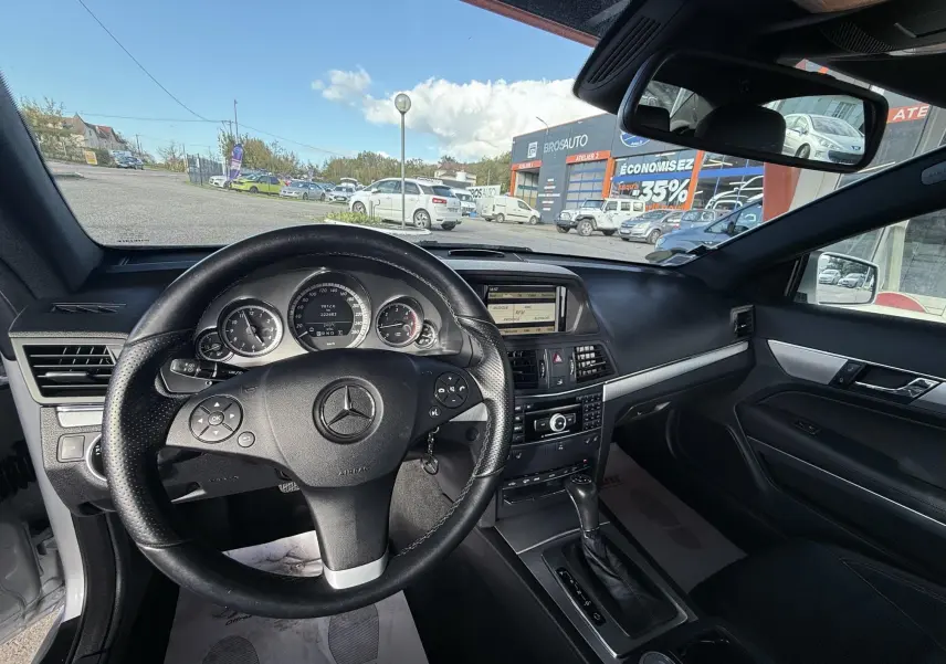 Vue intérieure du poste de conduite d'une Mercedes Classe E 250 Coupé gris, avec volant cuir et tableau de bord complet.