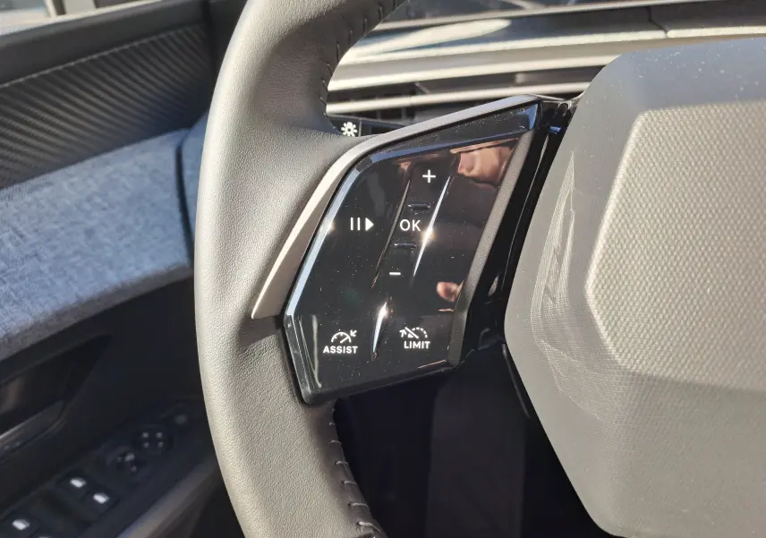 Gros plan sur les commandes gauche du volant en cuir gris du Peugeot 3008 hybride 2024, avec boutons assist et limiteur.