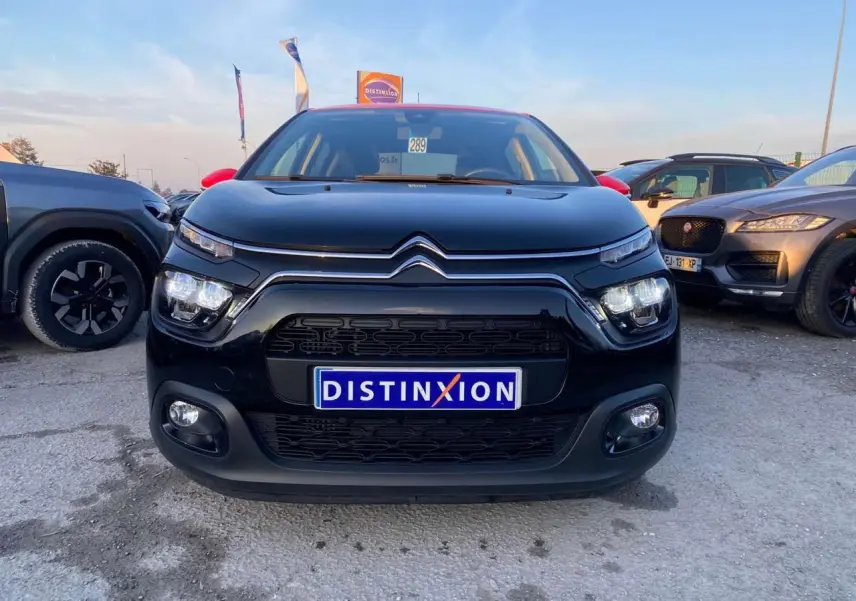 Vue frontale d'une Citroën C3 Shine 2023 noire avec toit rouge et projecteurs LED allumés sur parking.