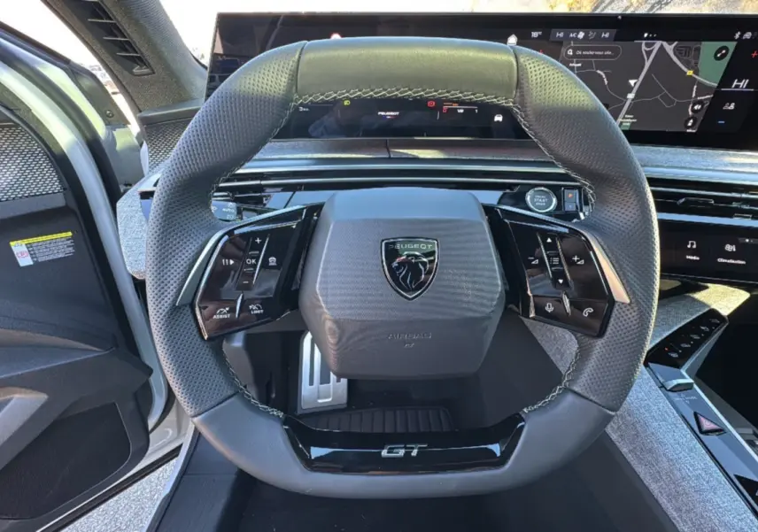 Vue rapprochée du volant cuir perforé noir avec logo Peugeot et inscription GT du 3008 Hybrid blanc okénite 2024.
