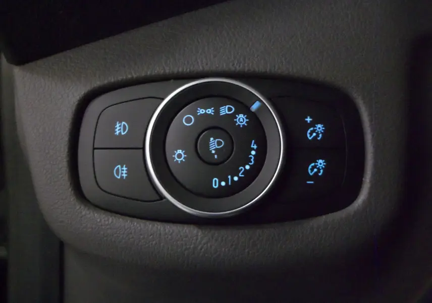 Gros plan sur le bouton de réglage des phares avec éclairage bleu dans l'habitacle gris du Ford Grand Tourneo Connect 2020.