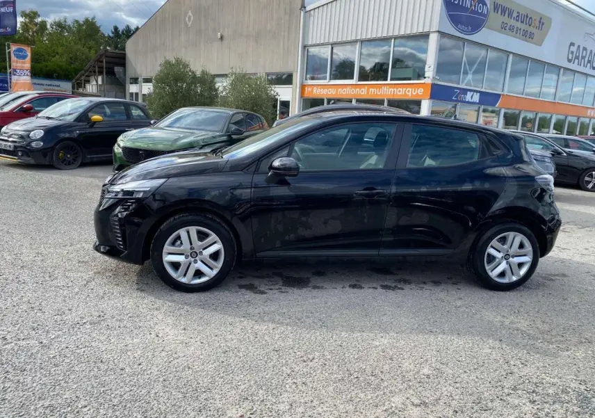 Profil côté gauche d'une Renault Clio 2025 noir étoilé garée devant un garage multimarque en extérieur.