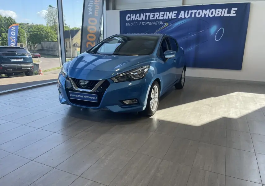 Nissan Micra bleu en 3/4 avant droit dans un showroom avec bannière Chantereine Automobile en arrière-plan.