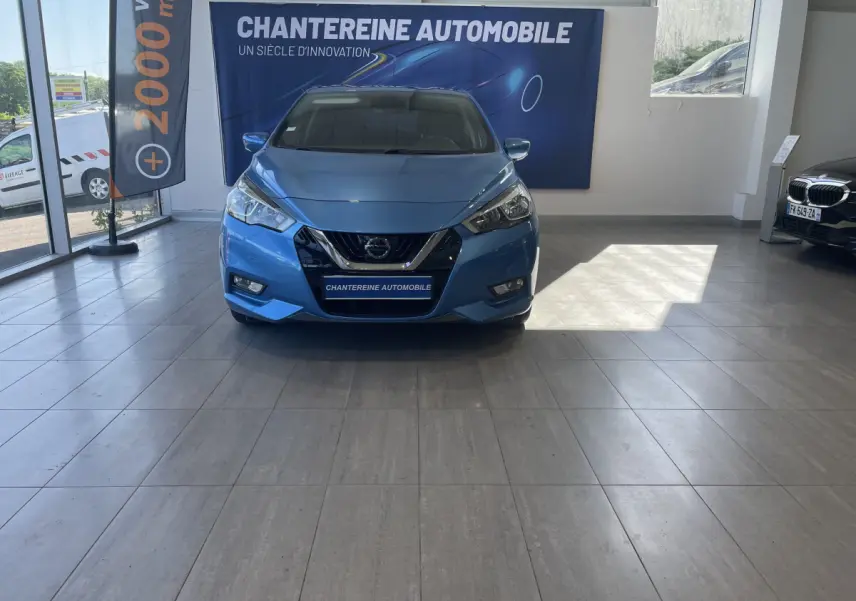 Vue de face d'une Nissan Micra IG-T 100 N-Connecta bleue exposée en showroom avec logo Nissan visible sur la calandre.